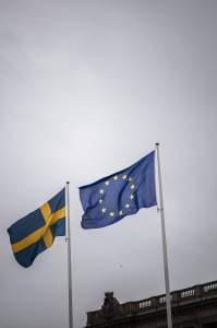 This photo shows the Swedish and European flags in front of the Swedish Parliament and the Royal Palace in Stockholm